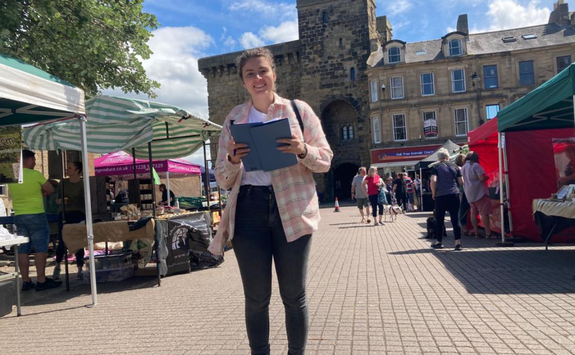 a person stands with a clip board taking research in a market square in Hexham